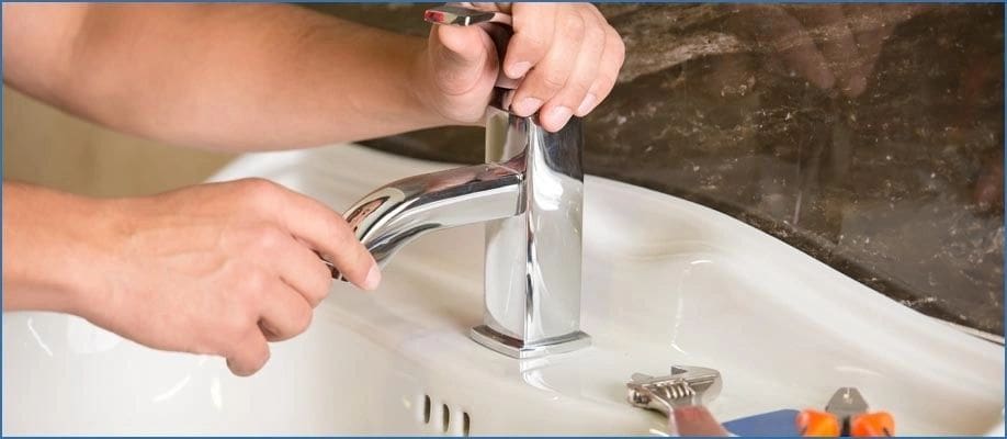 A person is fixing the faucet of a bathroom sink.